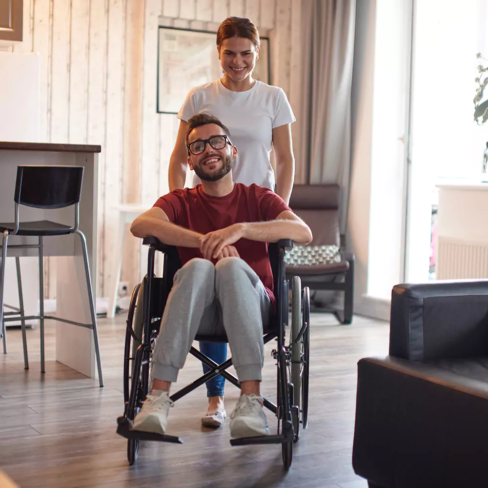 A paraplegic man in a wheelchair and his carer indoors