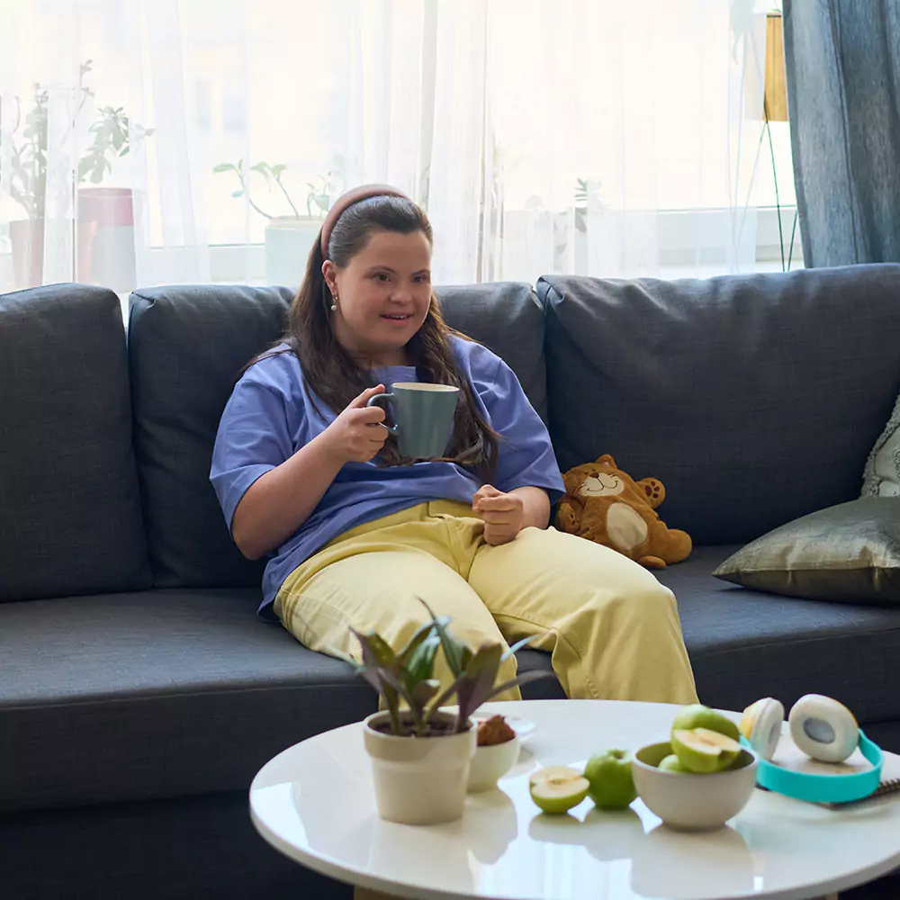 A down syndrome woman having a coffee indoors on the couch