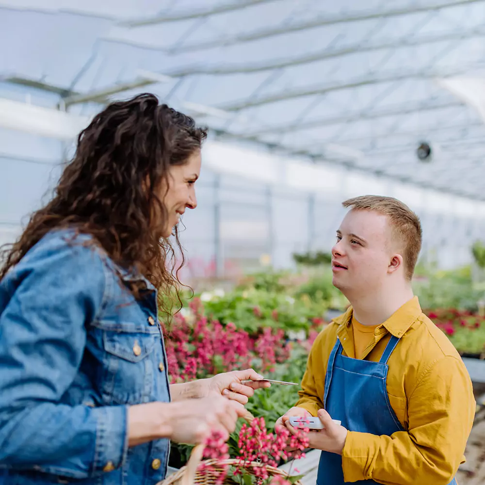 A down syndrome man and his carer in a nursery garden setting having a chat