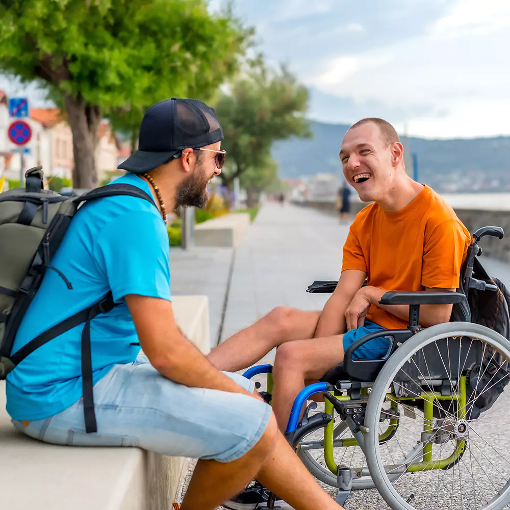 a disabled man in a wheelchair with his carer outdoors