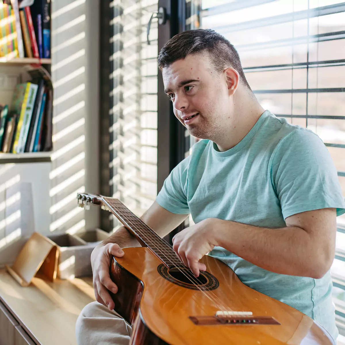 A down syndrome man playing his guitar indoors