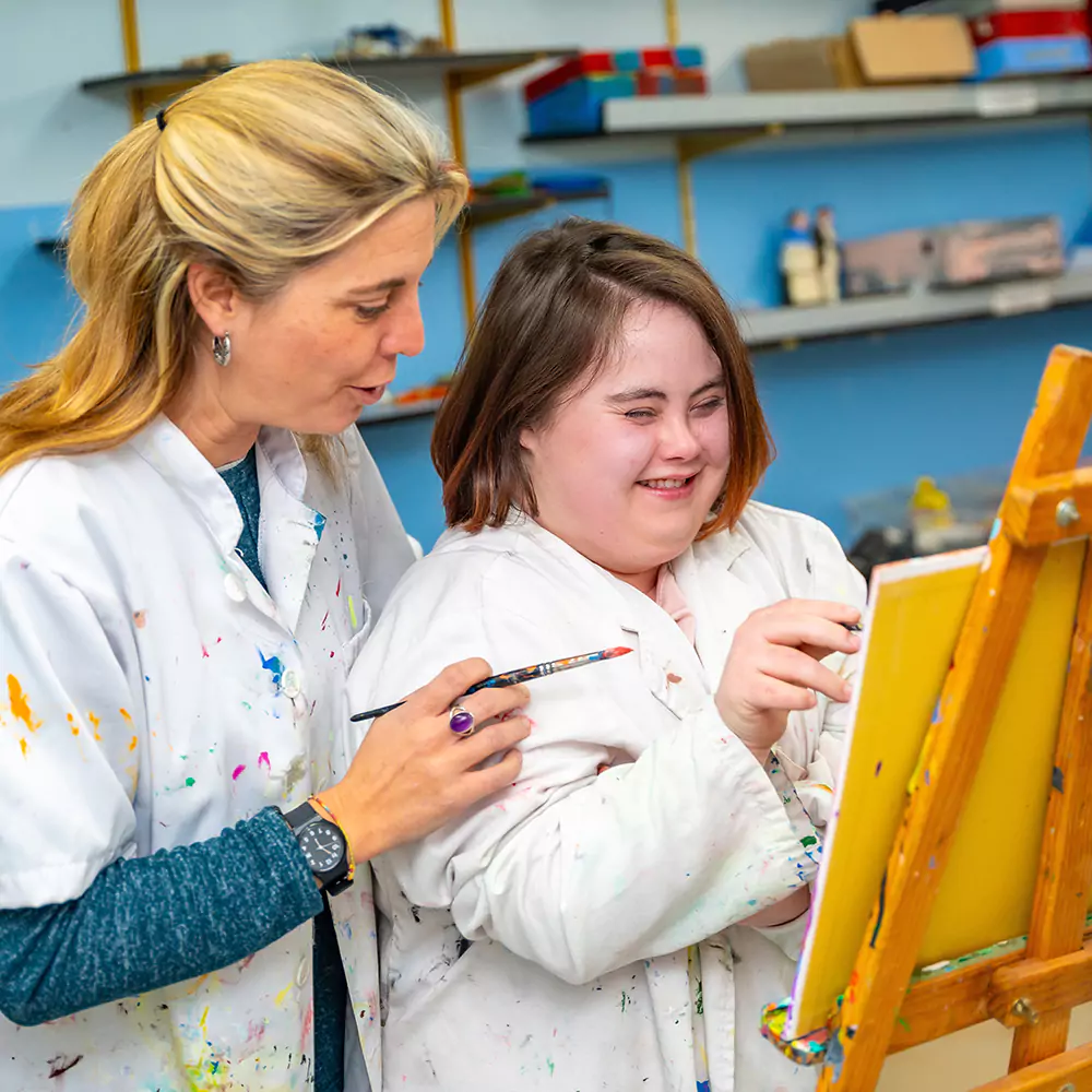 A down syndrome woman and her carer painting happily